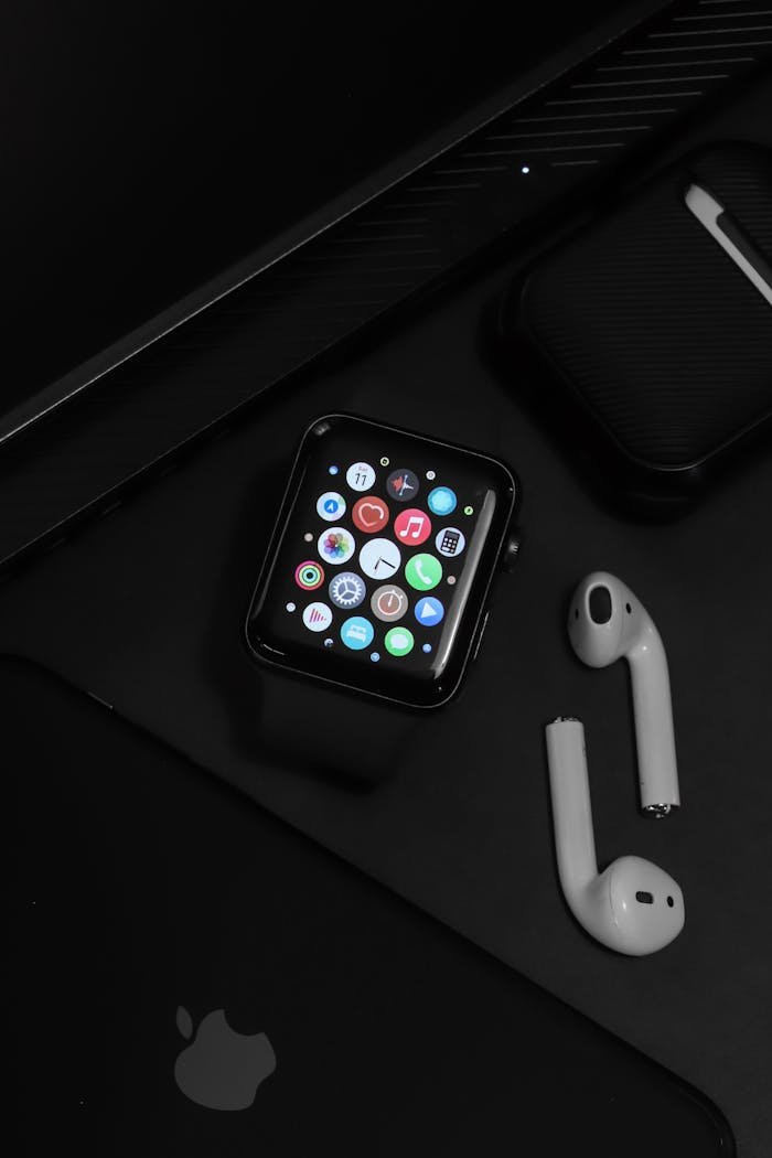 Stylish arrangement of modern tech gadgets on a dark surface, showcasing an Apple watch and AirPods.