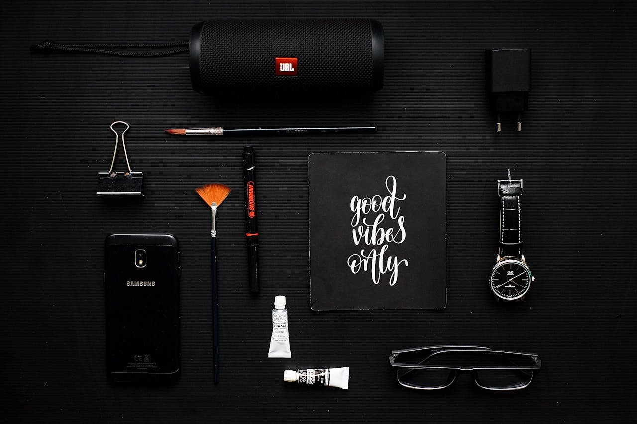 Creative flat lay of modern gadgets and art supplies on a dark surface, conveying a mood of style and inspiration.