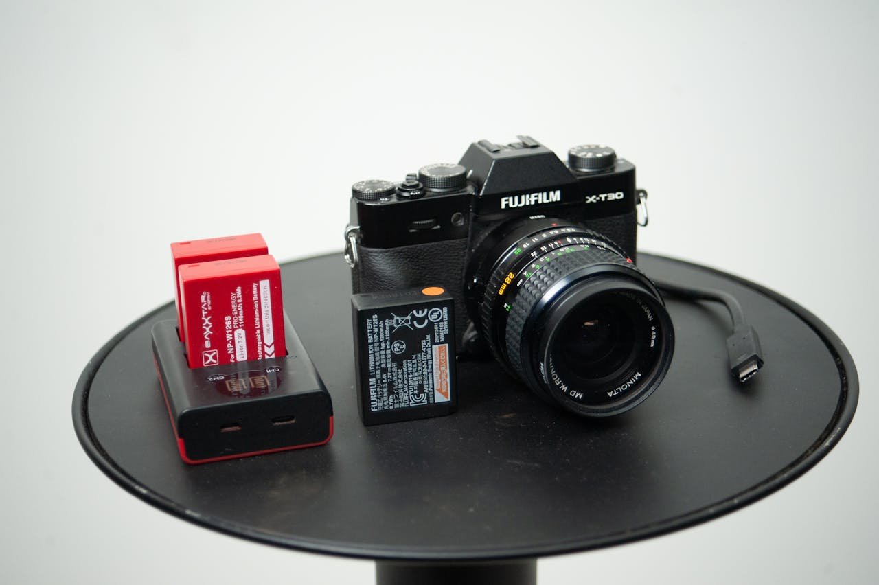 Close-up of a Fujifilm camera with lens, battery, and charger on a table.